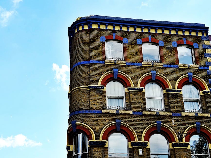 A multi-storey listed building with a classical façade, featuring large windows and decorative architectural details, situated on a paved street in Brixton. The building's exterior is painted white,